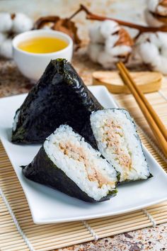 two pieces of sushi on a white plate with chopsticks next to it