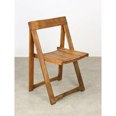 a wooden folding chair sitting on top of a cement floor next to a white wall