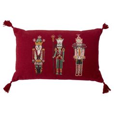 three nutcrackers embroidered on a red pillow with tassels and fringe