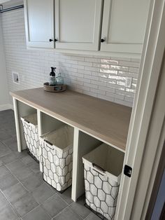 a kitchen with white cabinets and storage baskets on the counter top in front of it