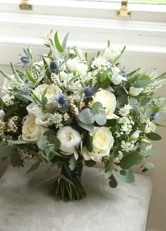 a bouquet of white flowers and greenery on a table next to a windowsill