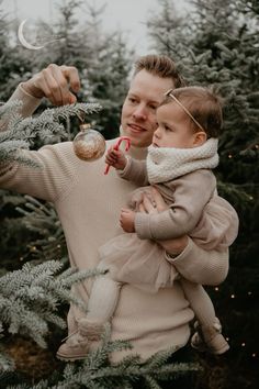 a man holding a small child in his arms while standing next to a christmas tree