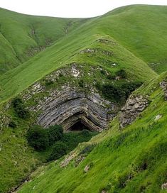 a green hillside with a cave in the middle and grass growing on it's sides