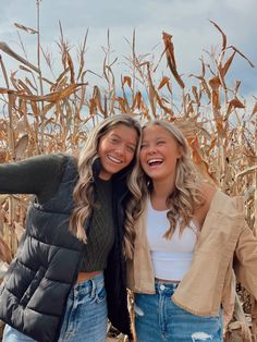 two young women standing in front of a corn field smiling at the camera with their arms around each other