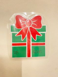 a green and red gift box with a bow on it's side hanging from the wall