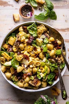 a bowl full of pasta salad with spinach, bacon and lettuce on the side