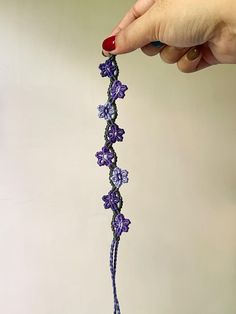 a woman is holding a crocheted purple flower in front of her face and hand