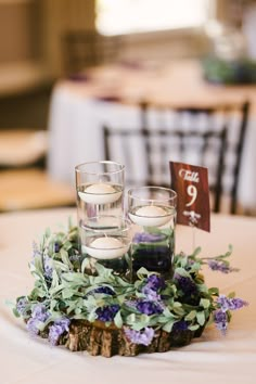 two candles are placed on a piece of wood with flowers and greenery around it