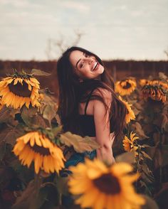 a woman standing in a field of sunflowers with her eyes closed and smiling