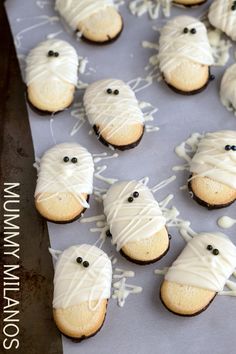 cookies decorated with white icing and black eyes are arranged on a baking sheet to look like ghost faces