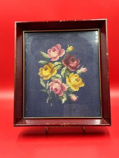 a cross - stitch picture with flowers in it on a red tableclothed surface