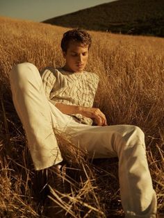 a man sitting in the middle of a field with his legs crossed and wearing white pants