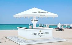 a white bar on the beach with an umbrella over it that says moet & chandon