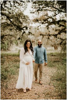 a pregnant woman and man walking through an oak tree lined path in front of some trees