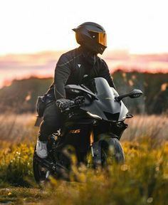 a man riding on the back of a black motorcycle down a lush green field covered in yellow flowers