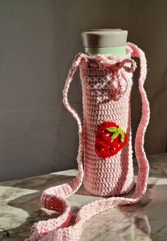 a crocheted strawberries bottle cover is shown on a marble table with a pink strap