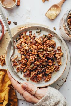 a person holding a plate with granola on it next to bowls and spoons