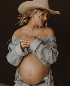 a pregnant woman wearing jeans and a cowboy hat poses for the camera with her hands on her stomach