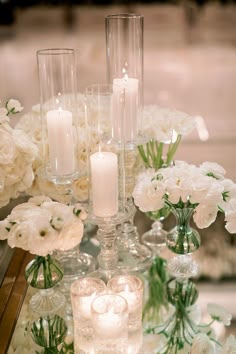 white flowers and candles are arranged in glass vases