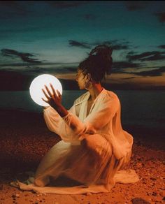 a woman sitting on the ground holding a white ball in her hands at night time