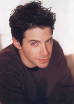 a young man with blue eyes is posing for a photo in front of a white wall