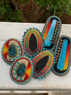 several pieces of colorful beaded hair combs on a white wooden bench with trees in the background