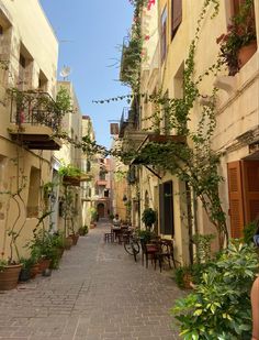 an alley way with tables and chairs lined up along the side of each building, surrounded by greenery