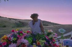 a man standing in front of a bunch of flowers with the sun setting behind him