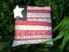 an american flag pillow sitting on top of some green grass with a white star in the center