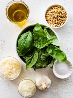 ingredients to make spinach salad laid out on a white surface with green leaves, garlic, and sunflower seeds