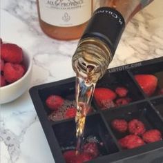 a bottle of wine being poured over raspberries