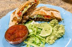 a blue plate topped with a cut in half sandwich next to lettuce and guacamole