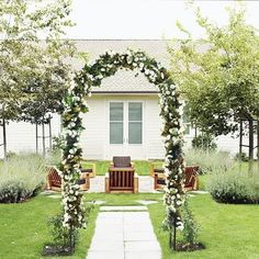 an outdoor wedding ceremony with flowers and greenery on the grass, in front of a white house