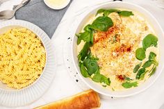 a bowl of pasta with spinach and cheese next to a plate of bread on a table