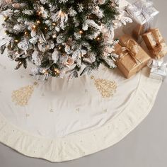 a christmas tree with presents under it on a white tablecloth covered in gold and silver wrapping