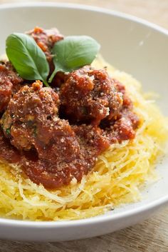 spaghetti with meatballs and sauce in a white bowl on a wooden table next to a fork