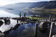 two people standing on rocks near the water