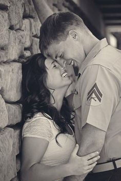 a man and woman standing next to each other near a stone wall with their arms around each other