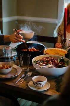 people sitting at a table with food and drinks in front of them, while one person holds a lit candle