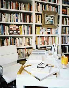 a room filled with lots of books next to a white chair and table in front of a book shelf