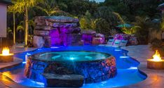 an outdoor hot tub lit up at night with fire lights on the sides and around it