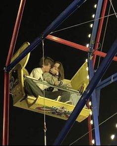 a man and woman sitting on a swing ride at night with lights in the background