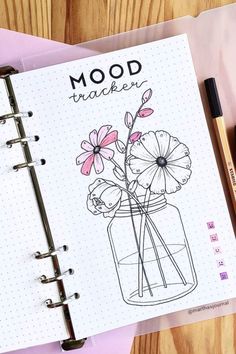 an open notebook with flowers in a jar on it next to a pen and pencil