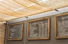 three framed menus hanging on the side of a wall under a shade cloth covered awning