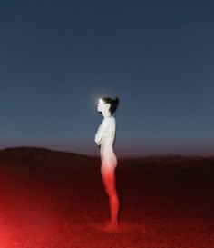 a woman standing in the middle of a desert at night with her head turned to the side