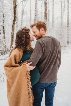 a man and woman standing next to each other in the snow with a blanket over them