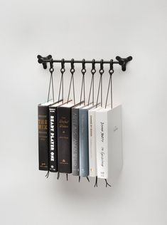 four books are hanging on the wall with black metal brackets and hooks attached to them