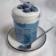 a glass jar filled with blueberries sitting on top of a saucer next to a spoon