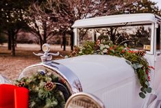 an old white car decorated with greenery and pine cones