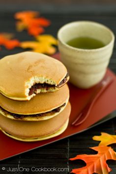 a stack of pancakes sitting on top of a red plate next to a cup of tea